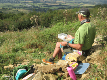 A walker rests on a stone mid-walk to enjoy their packed picnic lunch.